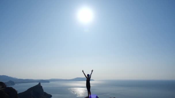 Shooting from above of a girl who conquered the top of a mountain above the sea and raised her hands up, enjoying the extraordinary beauty of nature and beautiful views of the sea, sun and rocks. - Footage, Video