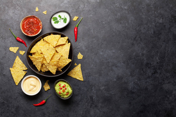 Mexické nachos chipsy s různými omáčkami - guacamole, salsa, sýr a zakysaná smetana. Horní pohled byt ležel na kamenném stole s kopírovacím prostorem - Fotografie, Obrázek