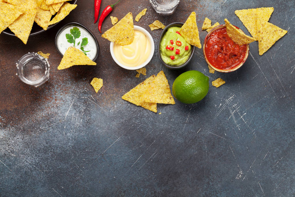 Mexikanische Nachos-Chips mit verschiedenen Soßen - Guacamole, Salsa, Käse und saure Sahne. Draufsicht flach auf Steintisch mit Kopierraum - Foto, Bild