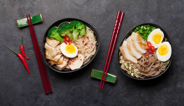 Asian noodle ramen soups with chicken, vegetables and eggs on stone background. Top view flat lay - Photo, Image