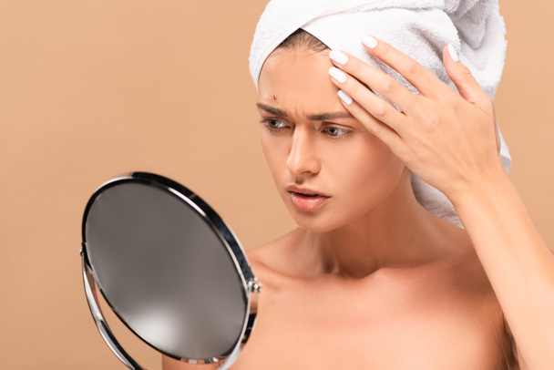 naked woman in towel looking at mirror and touching face with pimple isolated on beige  - Foto, imagen
