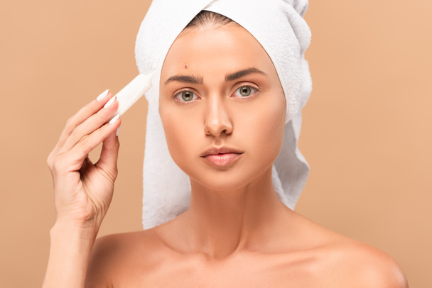 naked girl in towel holding treatment cream near face with problem skin isolated on beige  - Foto, afbeelding