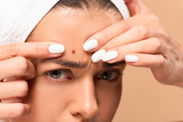 cropped view of young woman in towel squeezing pimple isolated on beige  - Photo, Image