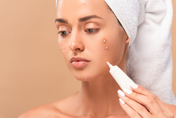 nude girl with acne on face holding treatment cream isolated on beige  - 写真・画像
