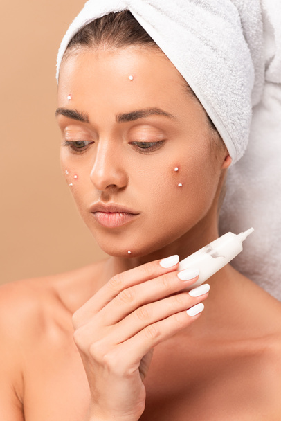 naked girl with acne on face holding tube with treatment cream isolated on beige  - Photo, Image