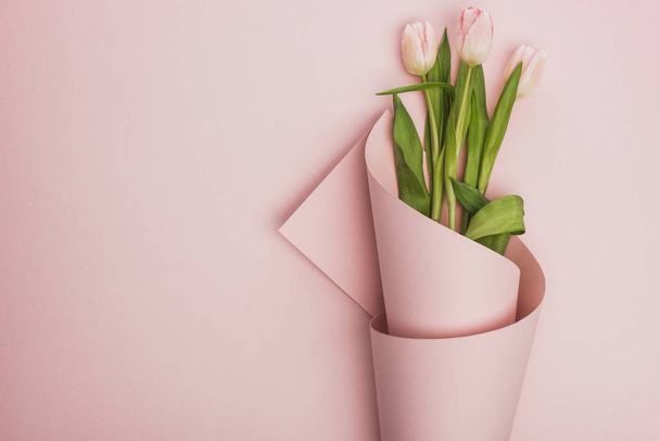 horní pohled na tulipány zabalené v papíru na růžovém pozadí - Fotografie, Obrázek