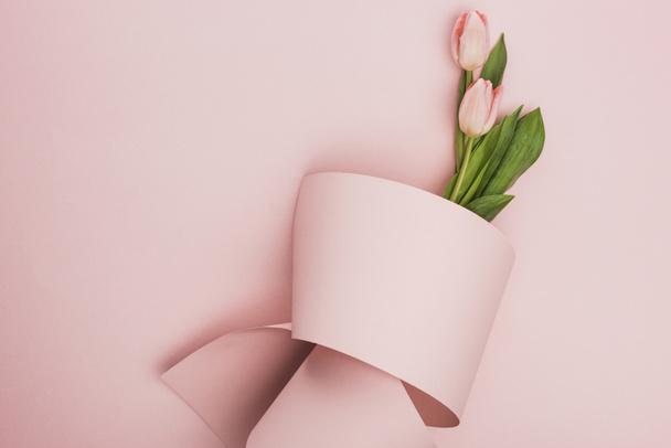 top view of tulip bouquet wrapped in paper swirl on pink background - Foto, Imagem