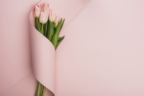 top view of tulip bouquet wrapped in paper swirl on pink background - Foto, afbeelding