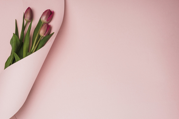 horní pohled na fialové tulipány zabalené v papírové víření na růžovém pozadí - Fotografie, Obrázek