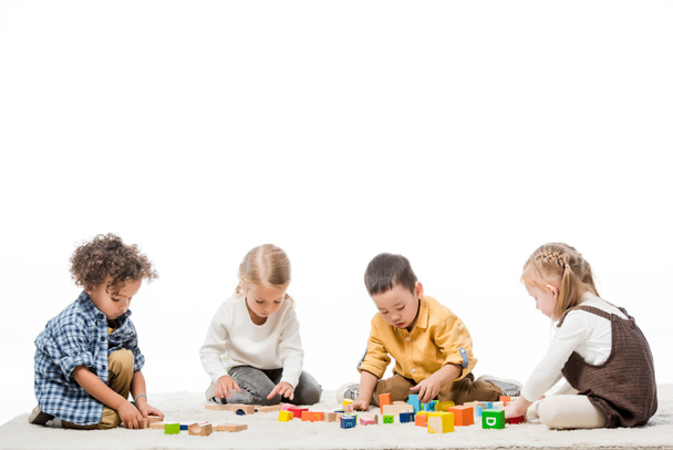 multiethnic kids playing with wooden blocks on carpet, isolated on white - Фото, изображение