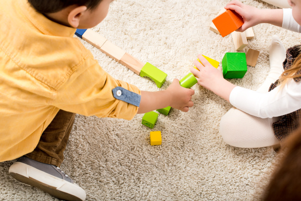 περικοπή άποψη των παιδιών που παίζουν με πολύχρωμα ξύλινα μπλοκ στο χαλί - Φωτογραφία, εικόνα