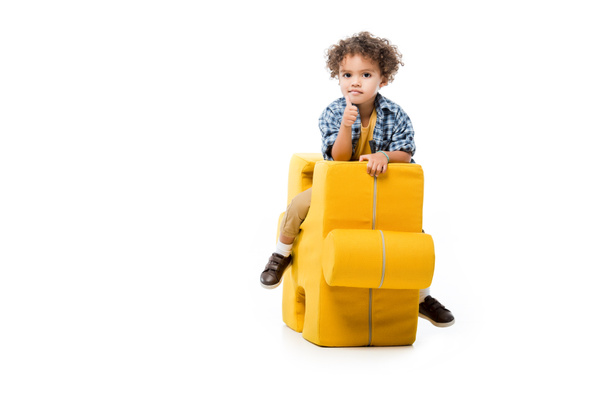 little african american boy showing thumb up and sitting on yellow puzzle chair, isolated on white - Fotografie, Obrázek