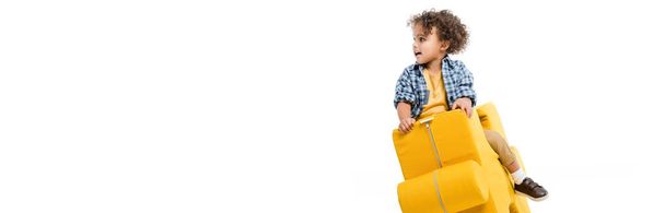 panoramic shot of little african american boy sitting on yellow puzzle chair, isolated on white - Photo, Image