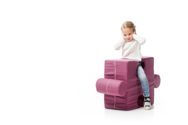kid closing ears while sitting on purple puzzle chair, isolated on white  - Фото, изображение