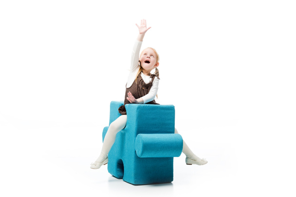excited child sitting on blue puzzle chair, isolated on white  - Фото, зображення