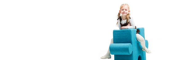 tiro panorámico de niño feliz sentado en la silla del rompecabezas azul, aislado en blanco
  - Foto, imagen