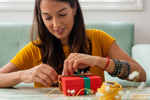 Жінка обгортає подарунки ручної роботи на столі вдома
 - Фото, зображення