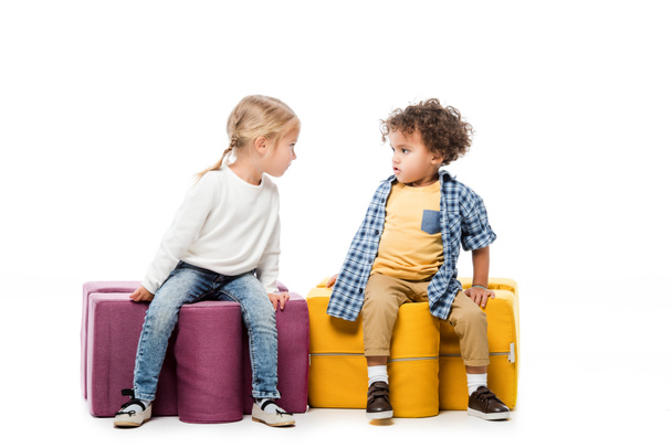 πολυπολιτισμικά ερεθισμένα παιδιά που κάθονται σε καρέκλες παζλ, σε λευκό - Φωτογραφία, εικόνα