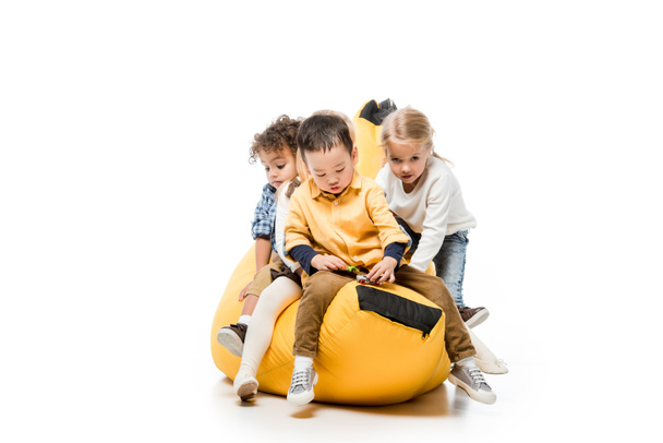 funny multicultural kids sitting on bin bag chair on white - Zdjęcie, obraz