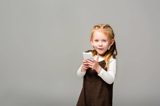 niño sonriente usando teléfono inteligente, aislado en gris
 - Foto, imagen