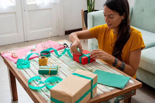 Frau verpackt handgefertigte Geschenke zu Hause auf den Tisch - Foto, Bild