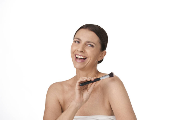 vrouw kijken in camera en lachen plezier houden van een make-up borstel in haar hand - Foto, afbeelding