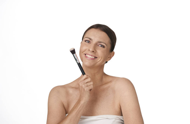kobieta patrząc szczęśliwy pewny siebie uśmiech trzymając pędzel makijaż w jej ręce na białym tle - Zdjęcie, obraz