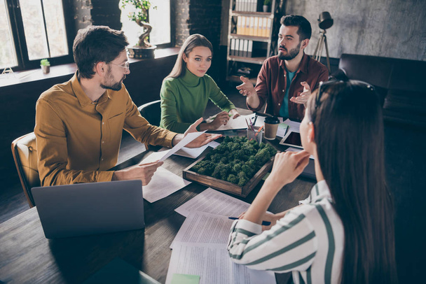 Company of four nice busy professional skilled businesspeople manager agent broker sitting around table discussing strategy at industrial loft interior style workplace workstation office - Foto, afbeelding