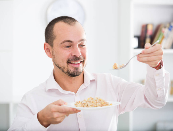 Positive young man eating porridge - Foto, afbeelding