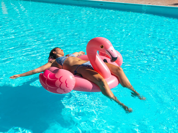 Молодая женщина расслабляется в бассейне на надувной розовой игрушке фламинго
 - Фото, изображение