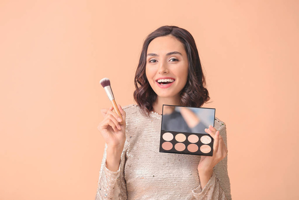 Beautiful young woman applying makeup on color background - Fotó, kép