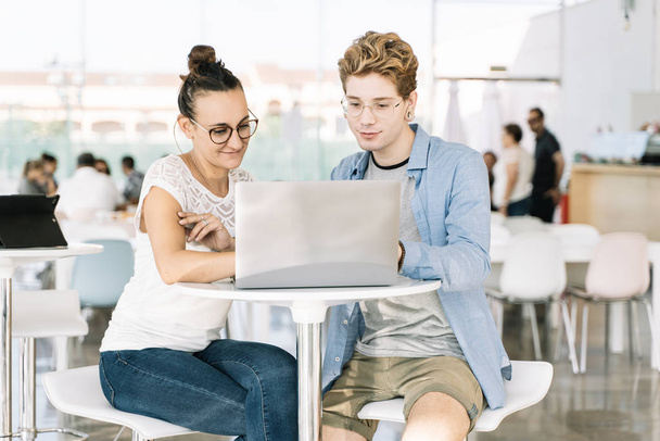 Giovane uomo con piercing e una ragazza con i capelli fino a lavorare insieme con un computer portatile in un coworking - Foto, immagini