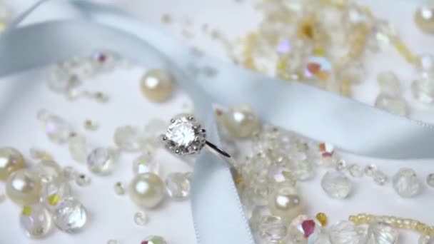 Samenstelling van een prachtige glanzende gouden trouwring met diamanten op een witte achtergrond, oorbellen, zilveren kralen, blauw satijnen lint. Huwelijksaanzoek voor 14 februari. - Video