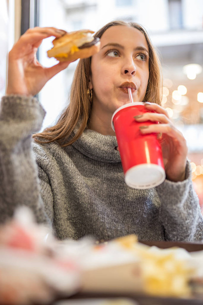 Söpö tyttö syö kahvilassa pikaruokaa kädessä
 - Valokuva, kuva