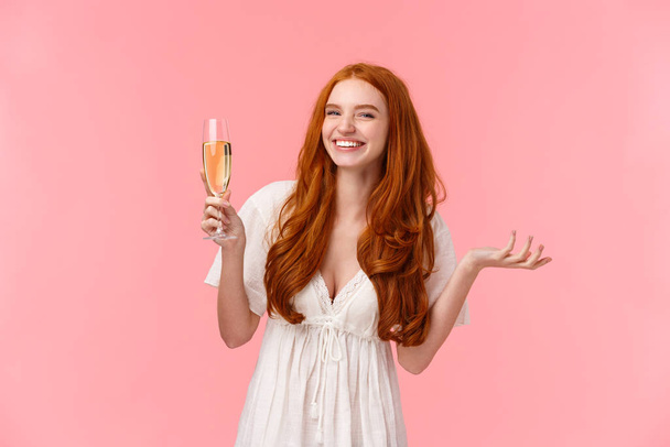 Piękny charyzmatyczny panna młoda czuje się szczęśliwa i radosna, świętując najlepszy dzień jej lfie, patrząc aparat zabawny, uśmiechnięty podnosząc szklanego szampana, picia i imprezowania, stojące różowe tło - Zdjęcie, obraz