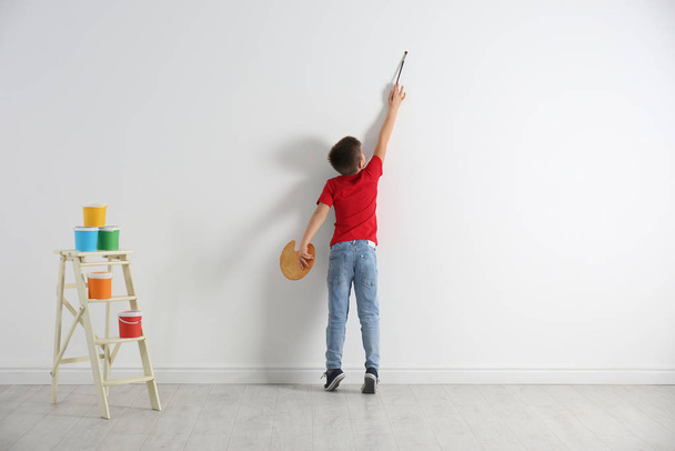 Little child painting on blank white wall indoors - Foto, Imagem