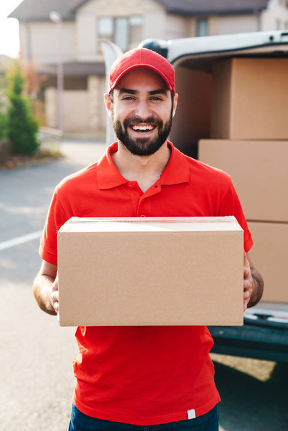 Image of smiling young delivery man standing with parcel box - Foto, afbeelding