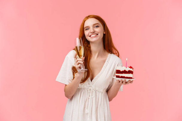 Прекрасна дівчина, яка святкує на її вечірці з друзями, чуючи сердечний тост, усміхаючись і дивлячись камеру милою, тримає скляне шампанське і торт на день народження, рожевий фон
 - Фото, зображення