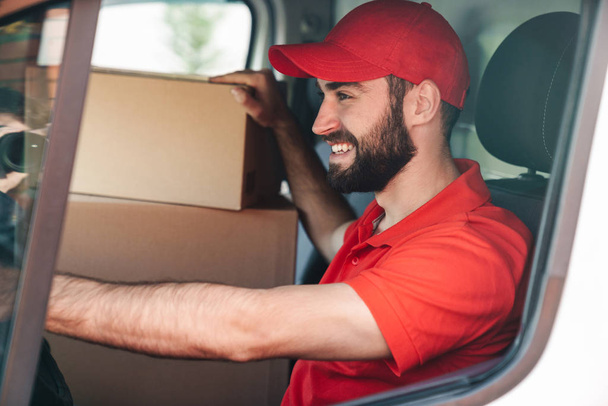 Image of happy young delivery man smiling and driving van - Foto, Imagen