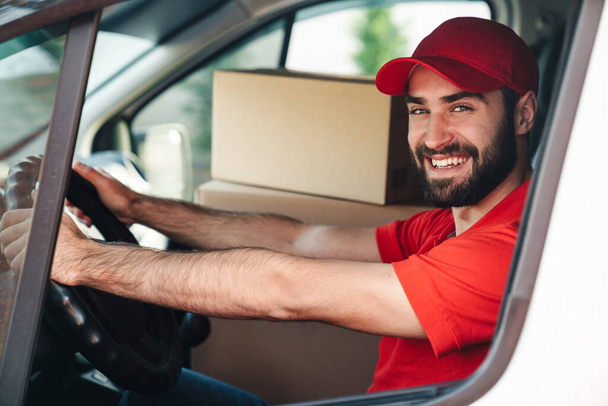 Image of happy bearded delivery man smiling and driving van - Fotoğraf, Görsel