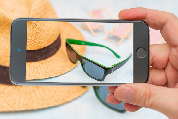 Набор для путешествий - солнцезащитные очки, соломенная шляпа. Фото смартфон. Смартфон в руке
. - Фото, изображение