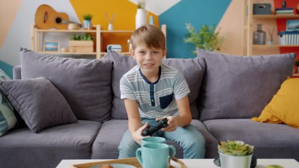 Portrait of happy boy playing videogame alone sitting on comfortable couch at home - Záběry, video