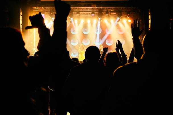 Multitud en un concierto de música, audiencia levantando las manos delante de luces de escenario brillantes
. - Foto, imagen