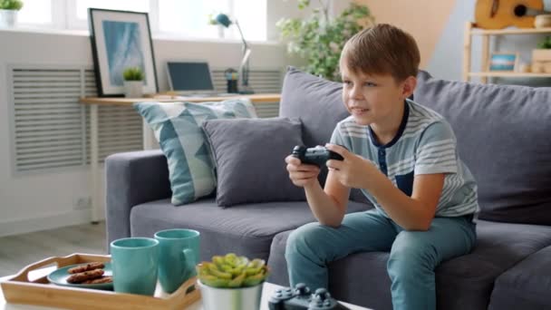 Gülümseyen küçük çocuk evde tek başına video oyunu oynuyor havalı bir aletle eğleniyor. - Video, Çekim