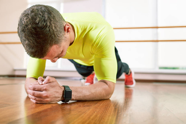 a man does an exercise plank in the hall on the floor opposite the window. Sports lifestyle, movement life. - Photo, Image