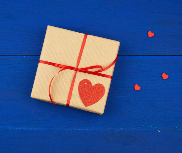 cadeau enveloppé dans du papier kraft brun et attaché avec un mince ribbo rouge
 - Photo, image