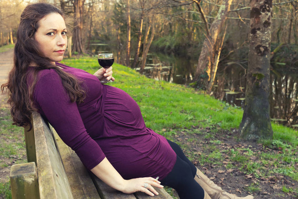 Беременная женщина с алкоголем и сигаретой в парке
 - Фото, изображение