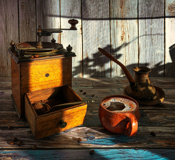 Kawa martwa natura. Filiżanka gorącej, aromatycznej kawy, stary ręczny młynek do kawy i cez do zaparzania napoju. - Zdjęcie, obraz