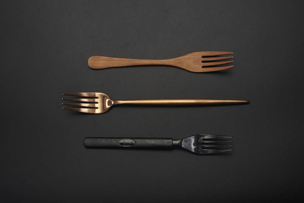 Drie verschillende materiaalvorken, houten vorken, lange steel goud metalen vorken, zwarte plastic vorken - Foto, afbeelding