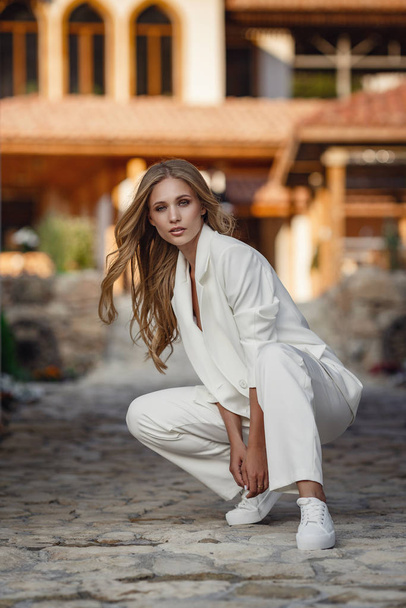 Outdoor full body fashion portrait of fashionable woman in white suit posing in street of east city - Zdjęcie, obraz